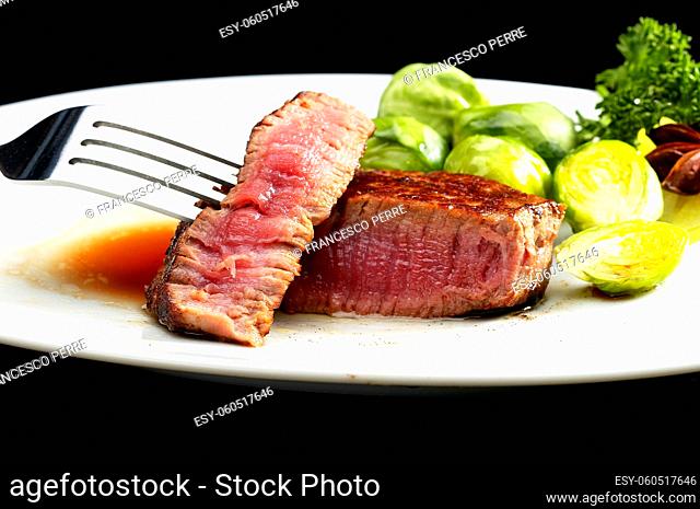 juicy filet mignon on plate with brussel sprout over black background