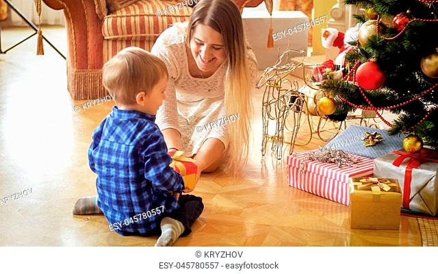 Toddler boy sitting on floor with mother and receiving Christmas gift