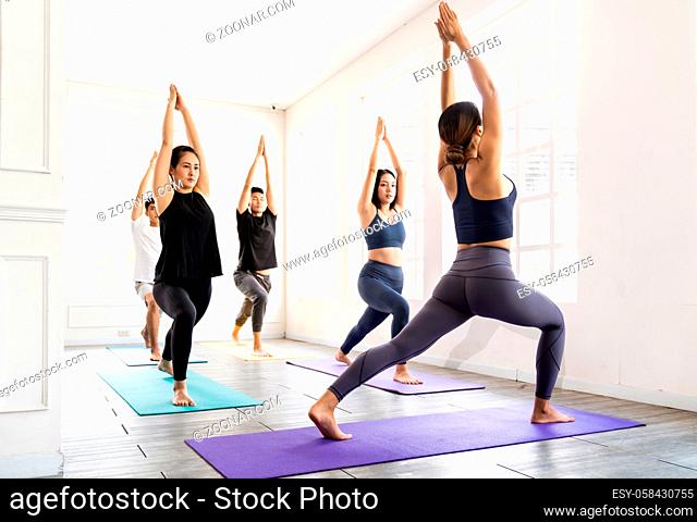 Group of young sporty attractive asian people practicing yoga lesson on Warrior and crescent pose with instructor coach in front in gym studio
