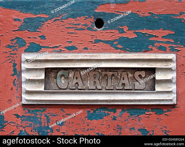 an old metal letterbox in a red wooden door with chipped peeling paint with the word cartas, translation from portuguese is mail