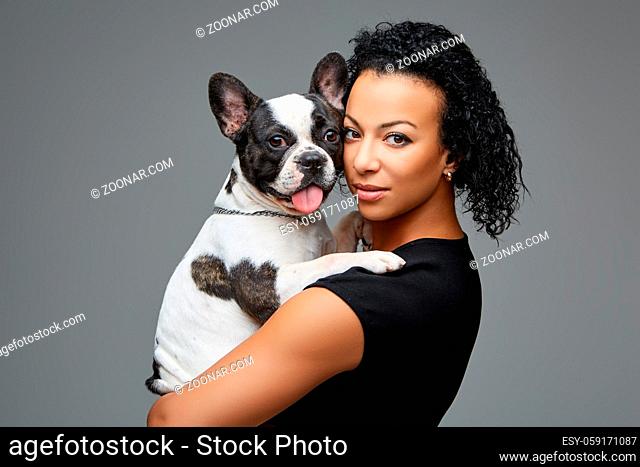 beautiful young woman holding french bulldog dog. studio shot over grey background. copy space