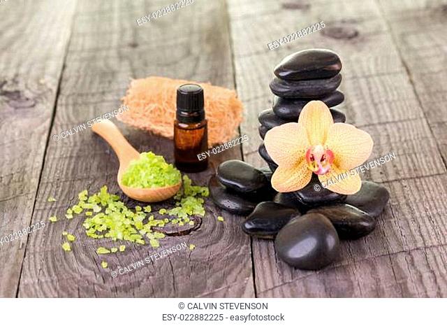 Yellow Moth orchid, essential oil and black stones on weathered deck