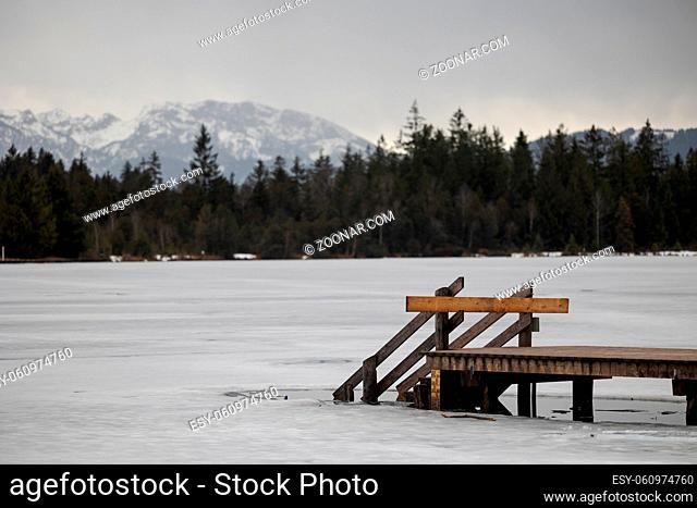 Barred wooden nose-piece on frozen lake in Upper Bavaria with Alps in background in winter with snow