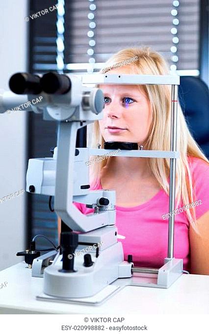 Optometry concept - pretty, young female patient having her eyes examined by an eye doctor