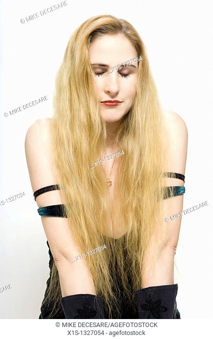A fair skinned woman with very long blond hair has her eyes closed as she kneels on the floor