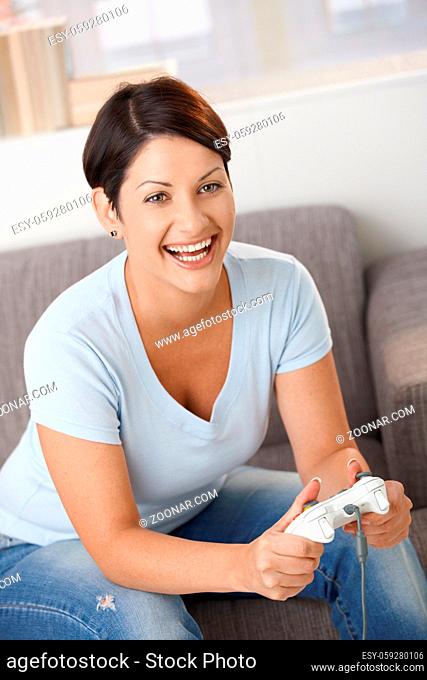 Excited young woman playing video game with controller, laughing