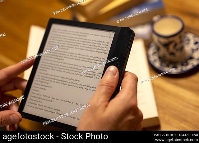 ILLUSTRATION - 17 October 2022, Berlin: A man holds an e-book reader in his hand while numerous paper books lie on the table in the background