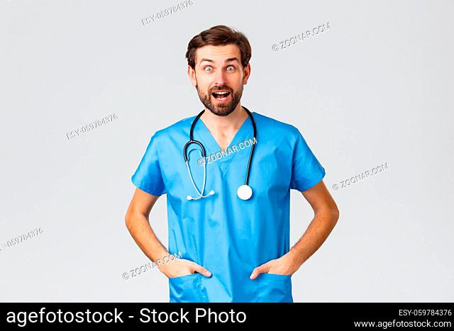 Covid-19, quarantine, hospitals and healthcare workers concept. Surprised and amused doctor in scrubs with stethoscope looking excited hearing good news