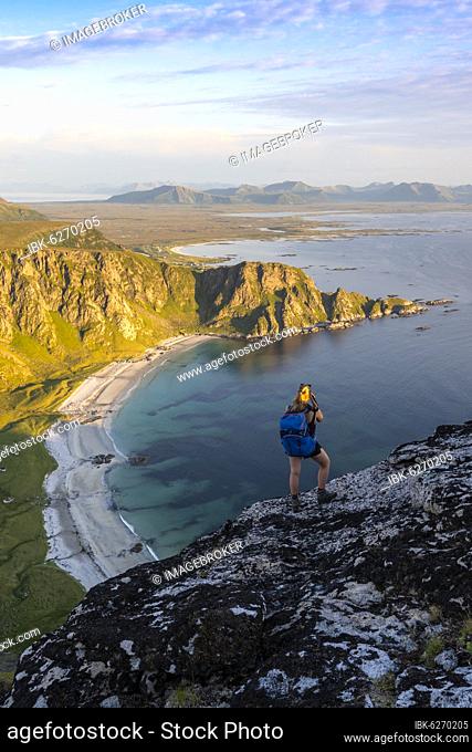 Hiker standing on rocks overlooking beach and sea, top of Måtinden mountain, near Stave, Nordland, Norway, Europe