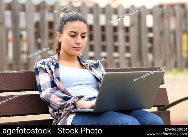 Serious teen using laptop in a bench in a park