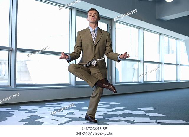 Meditating businessman in an empty office, sheets of paper on floor