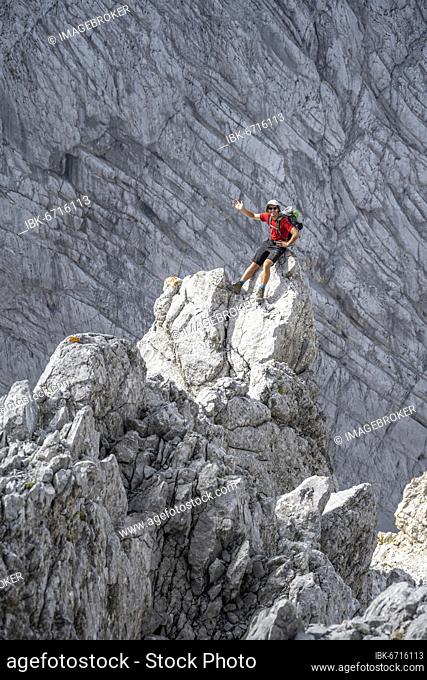 Young man sitting on rocks and waving, Rocky mountains and scree, Hiking to the Hochkalter, Berchtesgadener Alpen, Berchtesgadener Land, Upper Bavaria, Bavaria