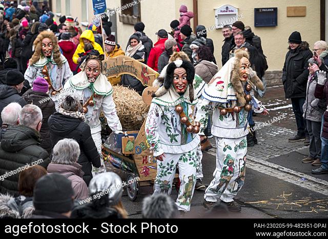 05 February 2023, Bavaria, Oberelsbach: Fools with wooden masks parade through the streets filled with spectators during the carnival procession