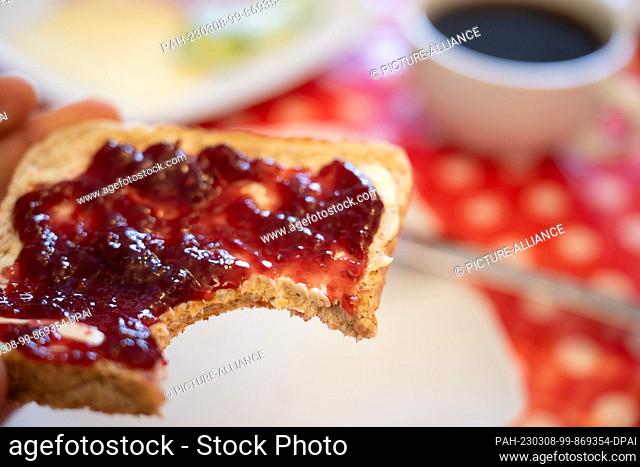 ILLUSTRATION - 06 March 2023, Hesse, Gießen: A man holds a piece of toast with raspberry jam. When asked about the ""most important meal"" of the day