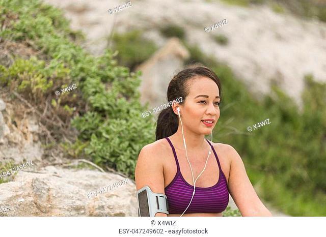 Runner woman resting after long run on the beach. Beautiful vivacious woman jogging on the beach with cloudy weather
