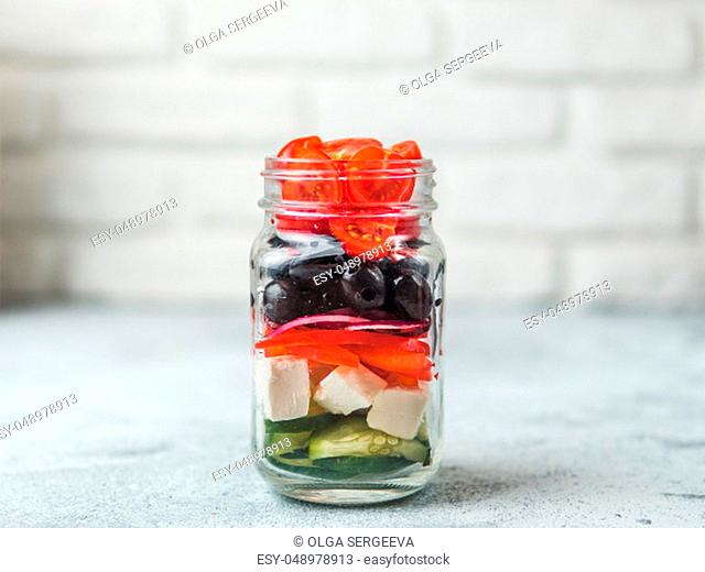 Greek Salad layered in glass mason jar on gray background, copy space. Trendy food. Idea, recept and concept of modern healthy food