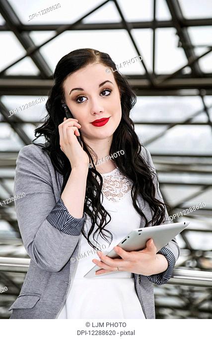 Attractive young millennial business woman on her cell phone in downtown office building; Edmonton, Alberta, Canada