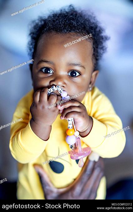 Baby girl chewing toy while held by man