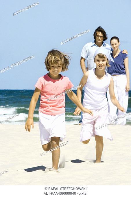 Girls running on beach while parents stand in background