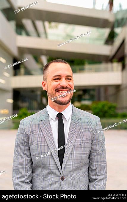 Portrait of handsome Hispanic bald bearded businessman wearing suit in the city streets outdoors