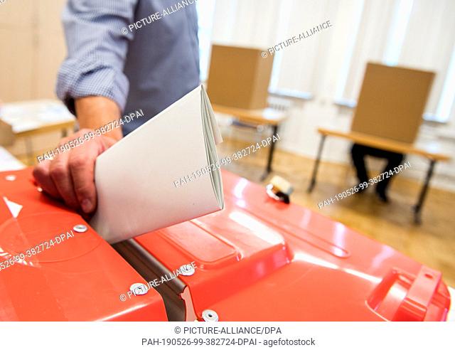 26 May 2019, Hamburg: ILLUSTRATION - An election assistant puts the ballot paper of a voter in a ballot box at a polling station for the Euro election into a...