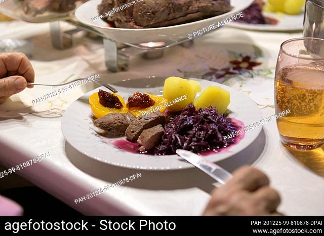 24 December 2020, Hamburg: Fallow deer loin with potatoes and red cabbage and cranberry jelly on apricots are ready to eat on a plate on Christmas Eve