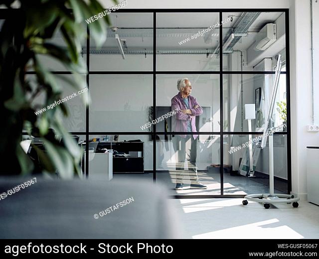Businessman with arms crossed looking away while standing at office
