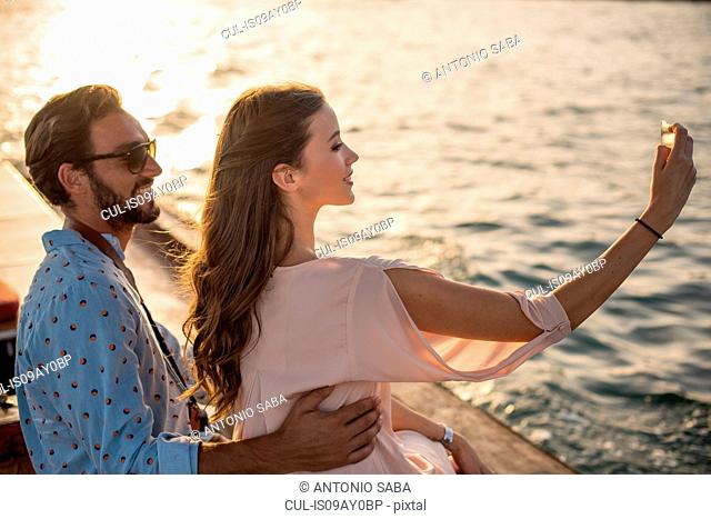 Romantic couple taking smartphone selfie on boat at Dubai marina, United Arab Emirates