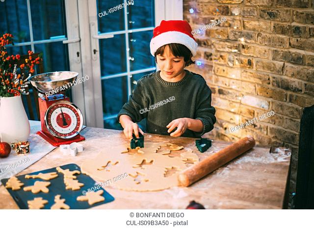Boy in Santa hat preparing Christmas cookies at kitchen counter