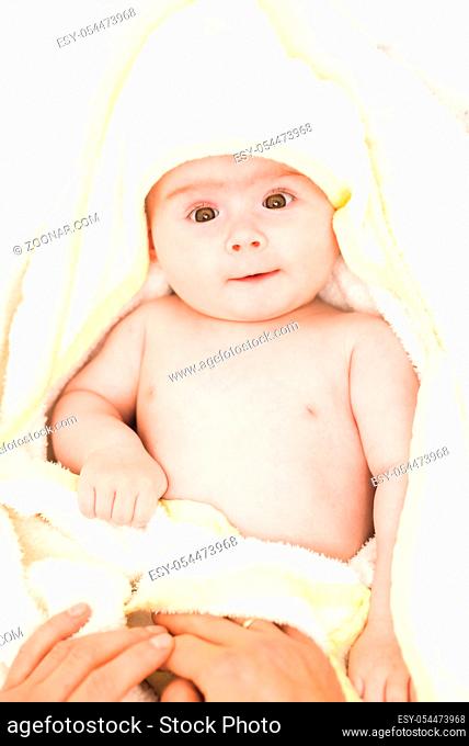 Adorable 6 months old Baby girl infant on a bed on her belly with head up looking into camera with her big eyes. Natural bedroom light
