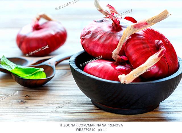 Old bowl with red onions on wooden table, selective focus