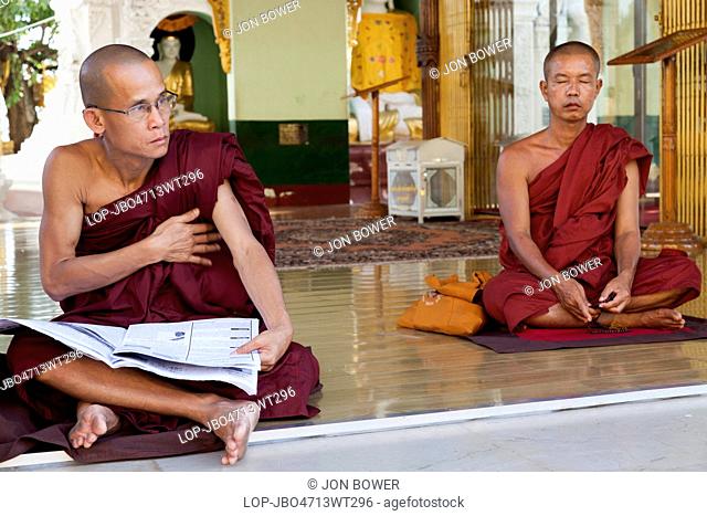 Myanmar, Yangon, Yangon. Two monks with one meditating and one reading a newspaper at the Shwedagon Pagoda in Yangon in Myanmar