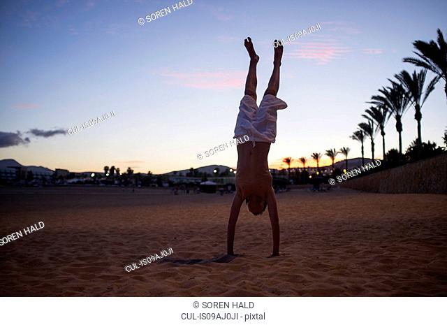 Silhouetted boy doing handstand on beach at dusk