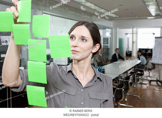 Germany, Munich, Businesswoman in office, putting sticky notes on glass pane