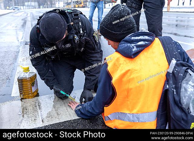 20 January 2023, Saxony, Dresden: A policeman uses olive oil to detach the hand of a ""Last Generation"" activist from the road
