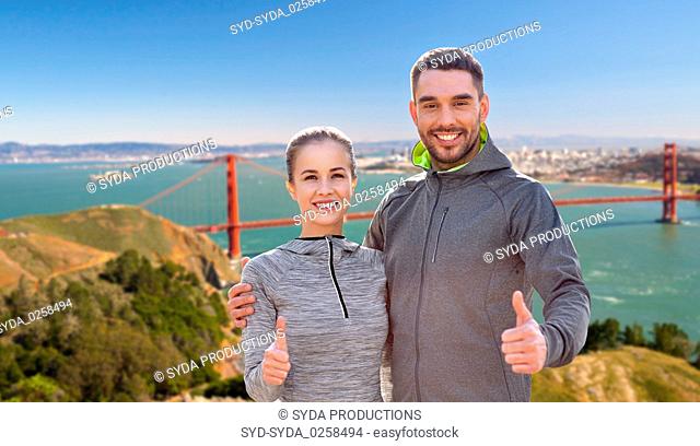 smiling couple in sport clothes showing thumbs up