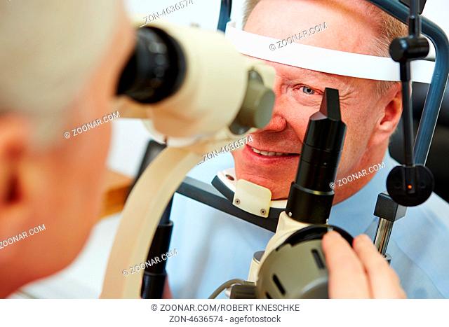 Lächelnder Mann schaut beim Optiker in eine Spaltlampe