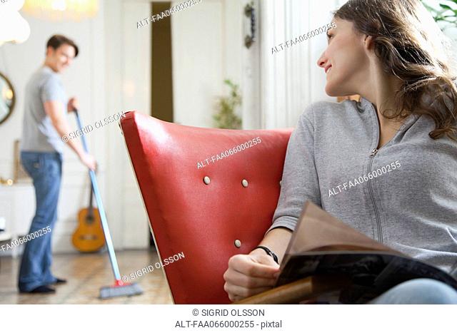 Woman smiling over shoulder at husband as he sweeps the floor