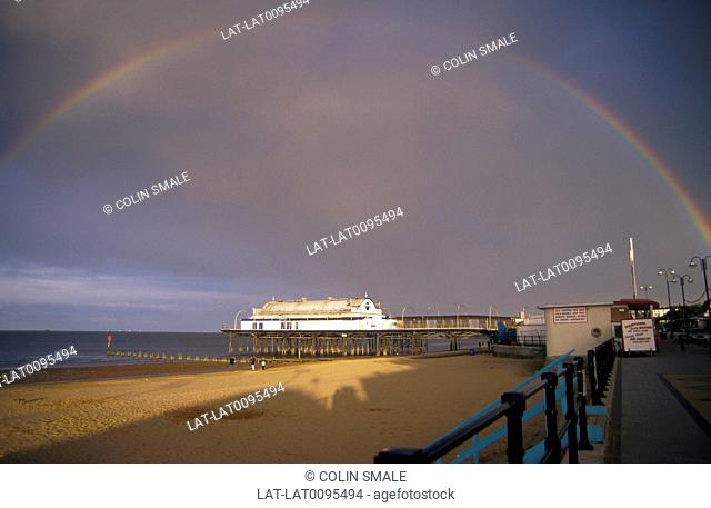 Sea. Pier. Beach. Rainbow in dark stormy cloudy sky