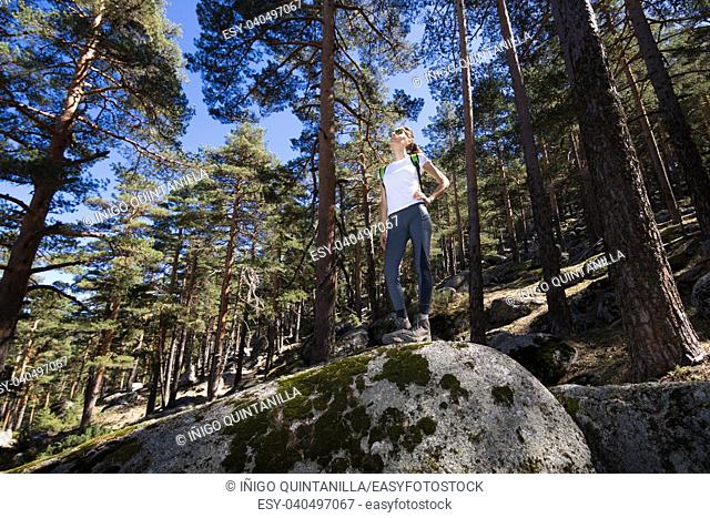 view from below of sport hiker woman with white shirt grey trousers standing posing on a great rock in the forest in Navacerrada mountain