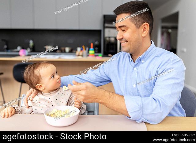 happy father feeding baby in highchair at home