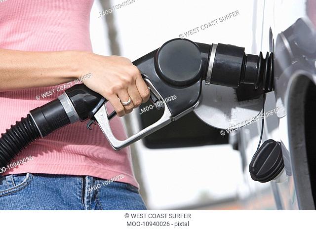 Woman by car with fuel pump mid section