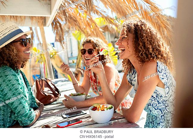 Happy women friends eating salad at sunny beach bar