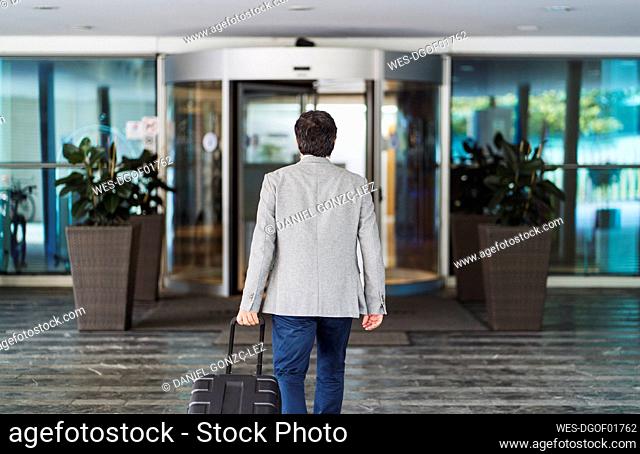 Businessman pulling wheeled luggage while leaving hotel