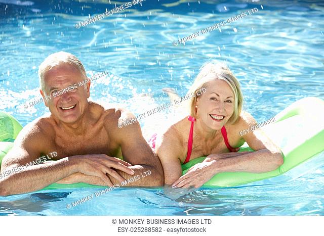 Senior Couple Relaxing In Swimming Pool On Airbed Together