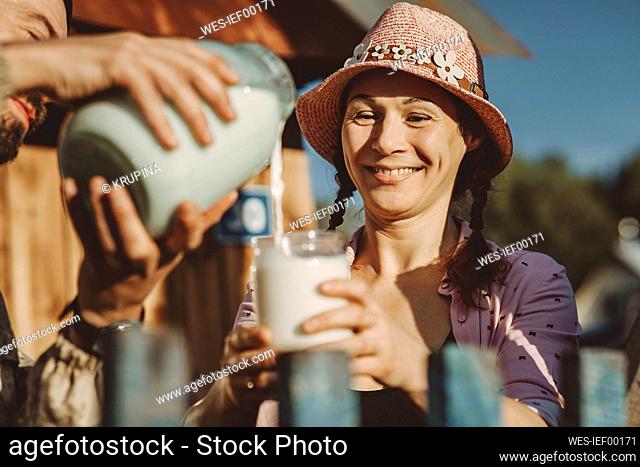 Happy girlfriend holding glass jar with boyfriend pouring milk