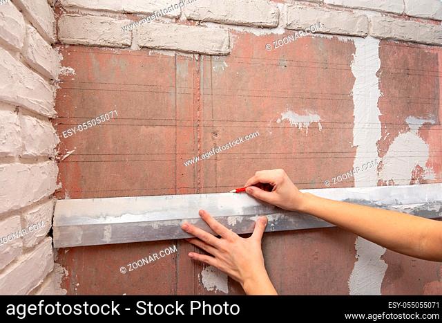 The girl draws on the wall of the line for the exact location of bricks