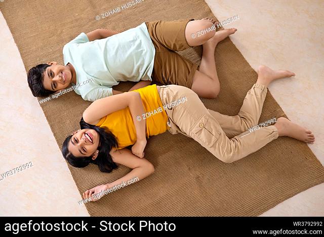 Overhead view of cheerful boy and girl lying down on floor in living room