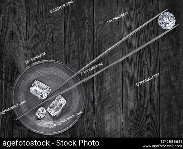 monochromatic image of a various cut diamonds in a working brass tray and tweezers