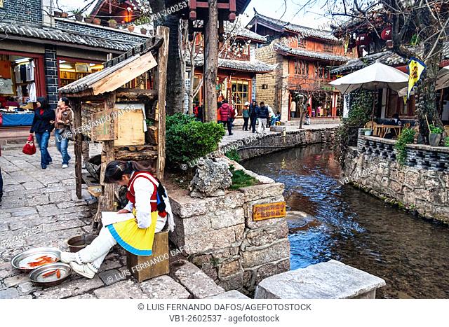 Naxi woman selling red carp by a waterway in old town Lijiang, Yunnan, China